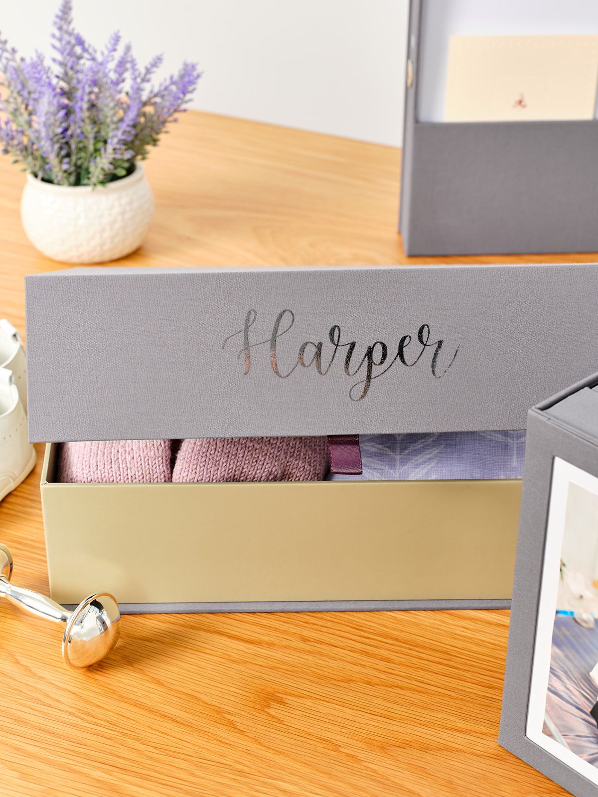 Slate color box personalized with the name ‘Harper’ and baby clothes inside.