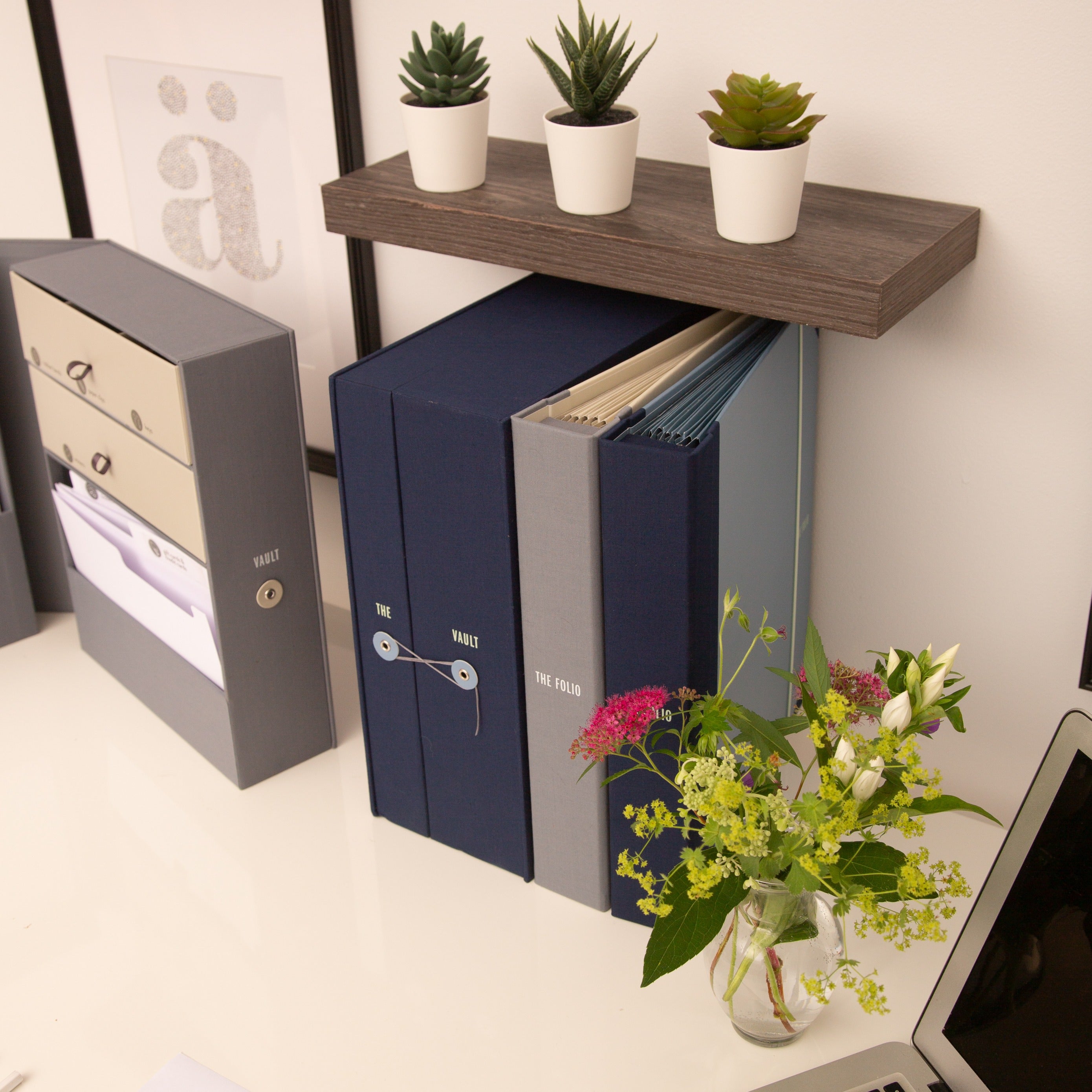 Savor organizers, folio and Vault, on table, sitting against wall, with plants and a frame in the background