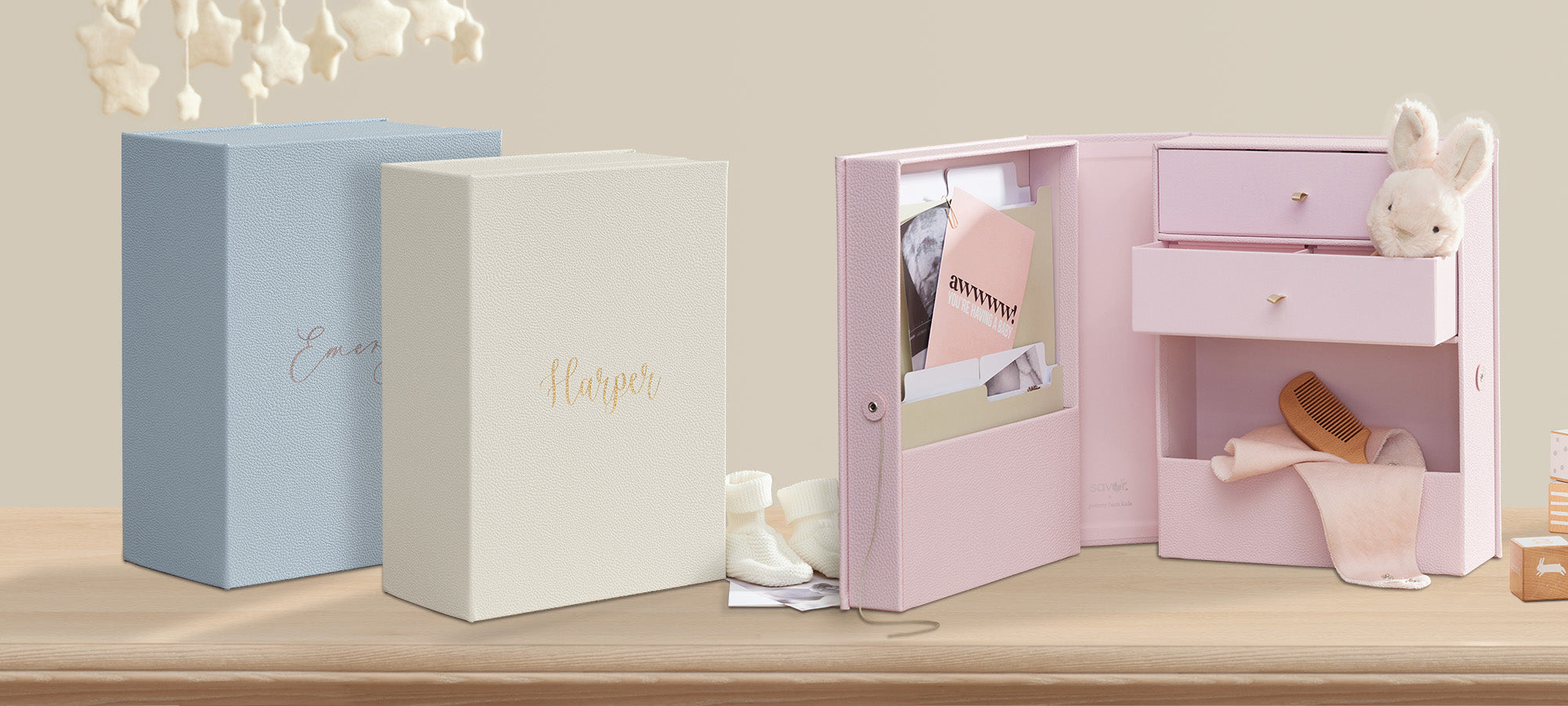 a closed ivory shagreen vault personalized with Harper in front of a sky closed shagreen vault personalized with Emersyn and an open pink shagreen vault with baby props