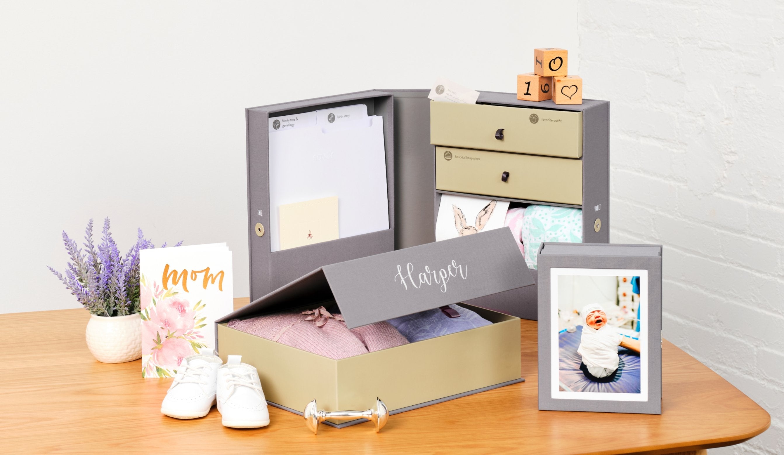 Slate color box set of a newborn with a baby picture on top and baby clothes inside over a table.