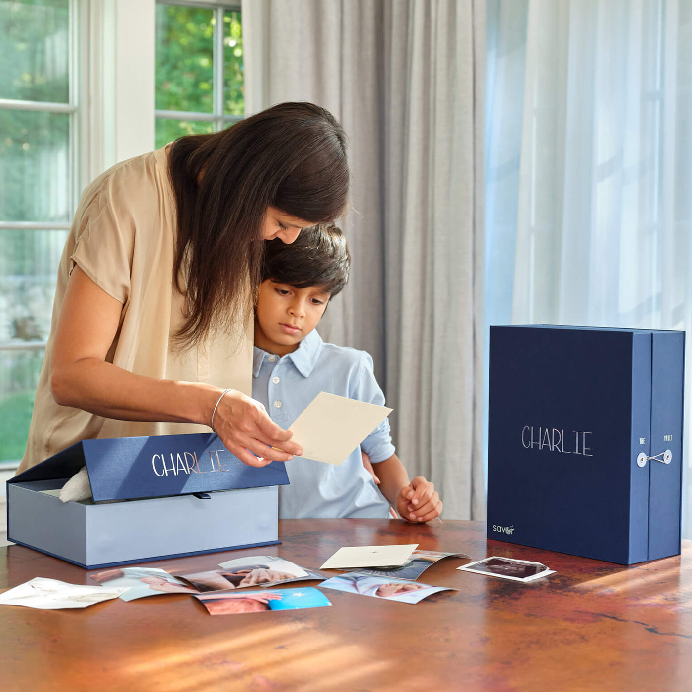 a woman and a kid looking at a photo with a something blue baby vault keepsake box and the overflow box. Both personalized with adelaide