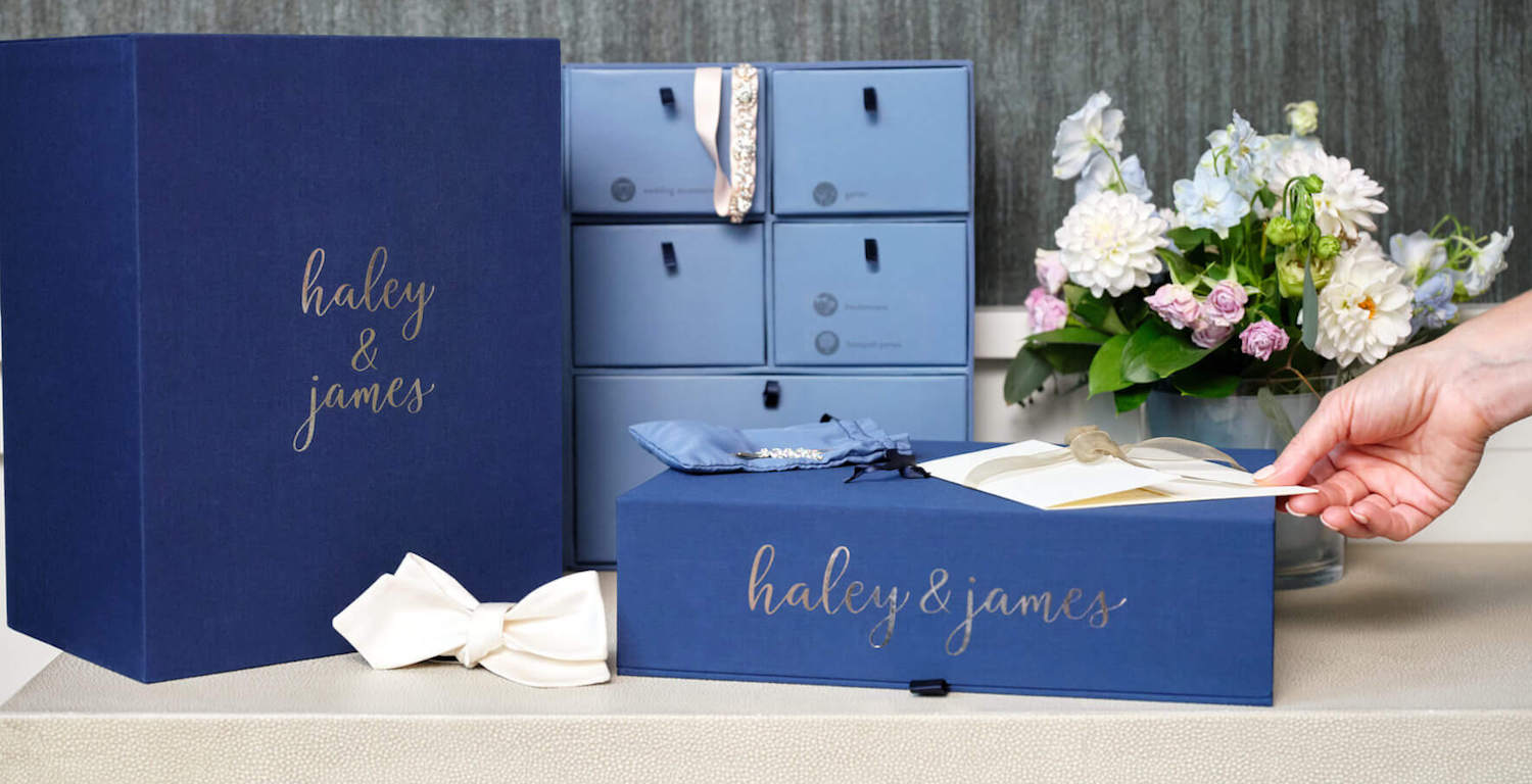 Set of blue organization boxes personalized with ‘Haley & James’, decoreted with flowers over a table.