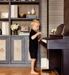 kid playing the piano with book shelf behind, with deluxe keepsake boxes on it.