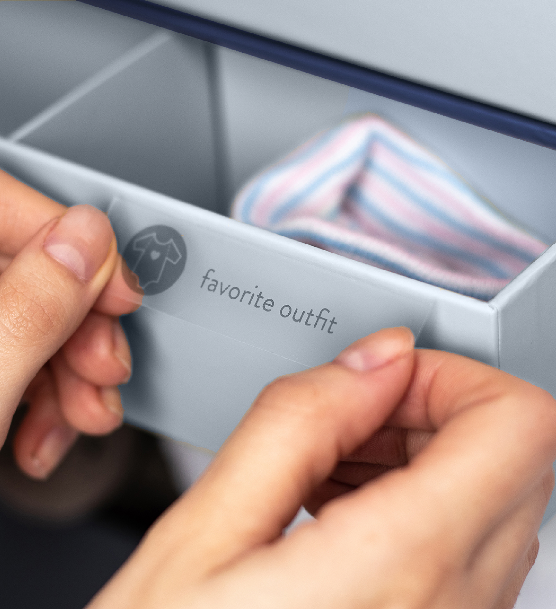 Close up of a drawer on a blue savor keepsake box, a hand applies a label that reads 'favorite outfit'