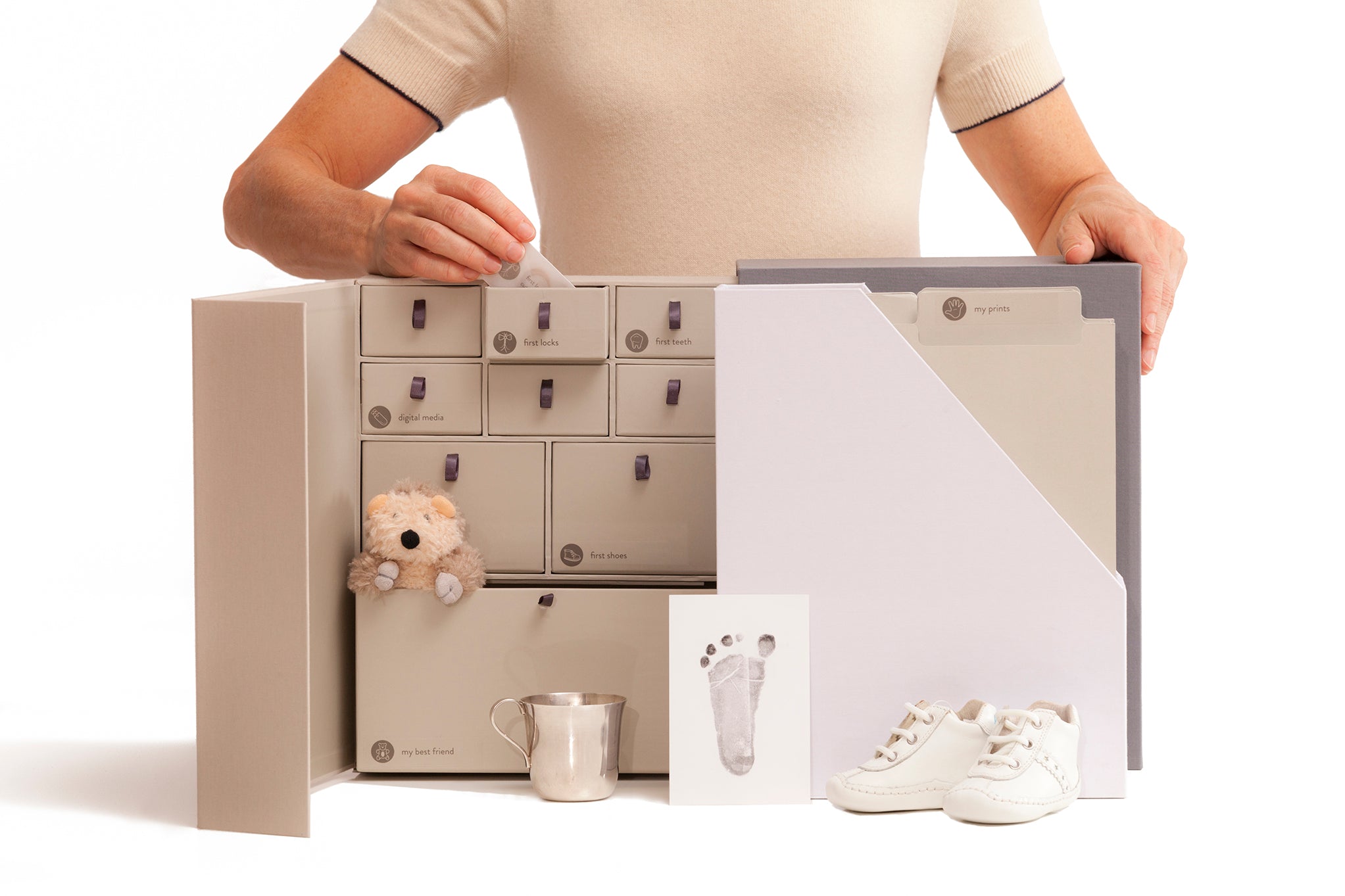 open slate babby deluxe keepsake box with baby props and someone putting a transparent envelope into a drawer.