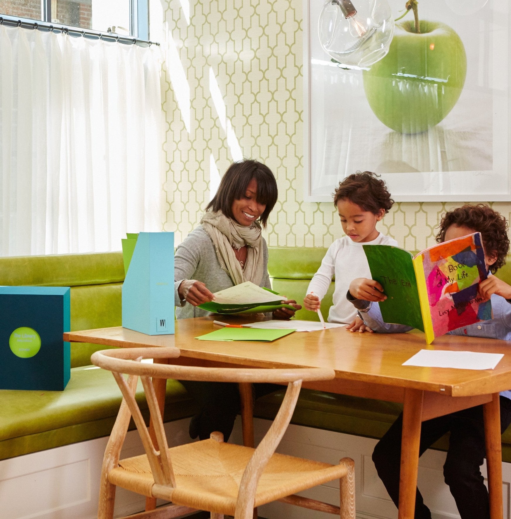 a woman and two kids sitting at a table looking at memories from an ocean school years deluxe keepsake box.