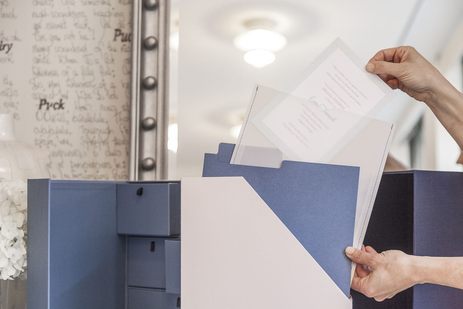 someone inserting a wedding invitation into a transparent envelope and the envelope into a something blue folder